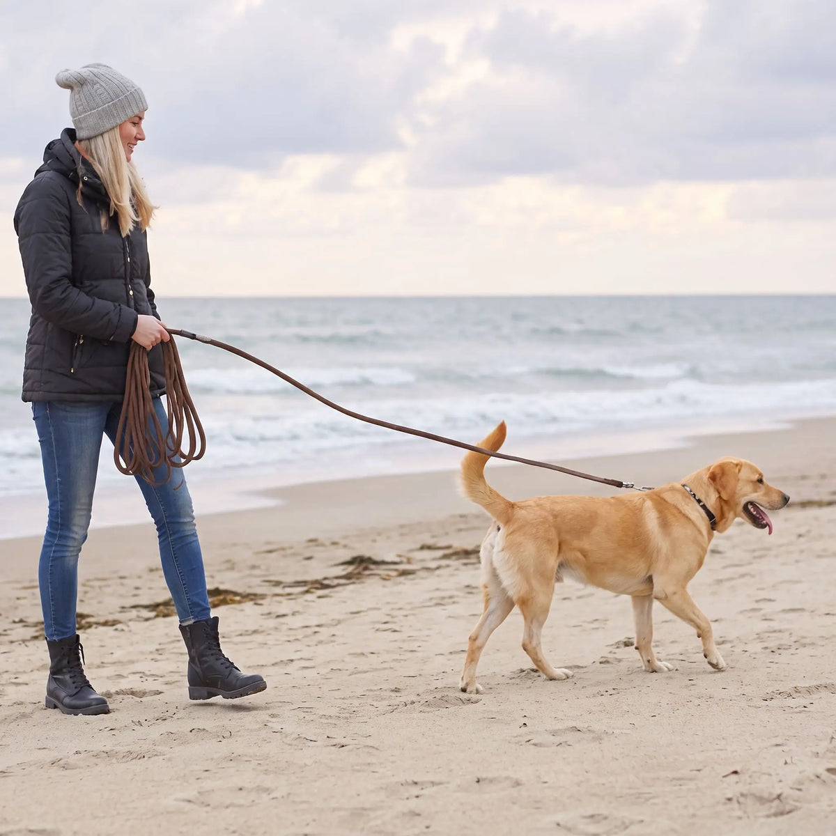 Femme qui promène son chien sur la plage avec la longe pour chien marron